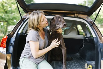Woman stroking Labrador Retriever in car trunk