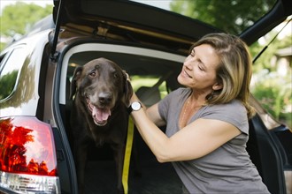 Woman with Labrador Retriever on leash in car trunk