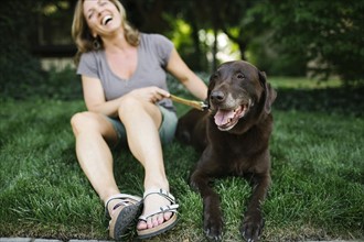 Smiling woman sitting on grass with Labrador Retriever