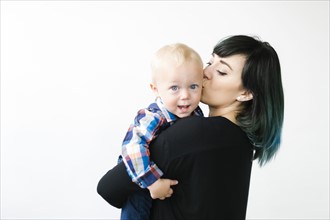 Portrait of mother kissing son (12-17 months) against white background