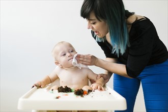 Mother cleaning baby boy (12-17 months ) sitting in high chair
