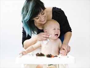 Mother cleaning baby boy (12-17 months) from cupcake