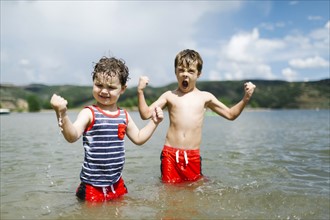 USA, Utah, Park City, Brothers (4-5, 6-7) flexing muscles while wading in lake