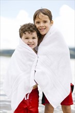 Portrait of brothers (4-5, 6-7) wrapped in towels standing by lake