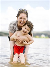 Portrait of laughing mother with son (4-5) wading in lake