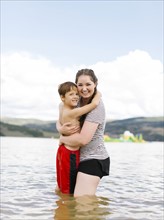 Mother with son (6-7) embracing while wading in lake