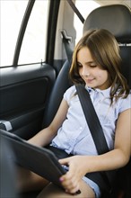 Girl ( 8-9) sitting in car and using digital tablet