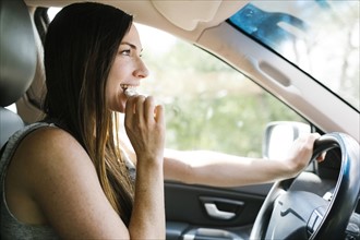 Smiling woman driving car and eating pretzel