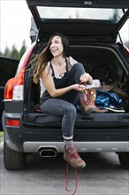 Smiling woman sitting in car trunk and tying hiking shoes