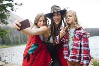 Outdoor portrait of mother with kids (6-7, 8-9) taking selfie by lake