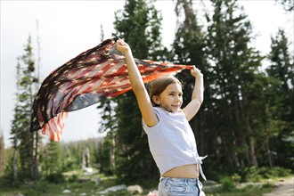 Girl (8-9) holding us flag in forest