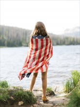 USA, Utah, Midway, Rear view of girl (8-9) wrapped in us flag standing by lake