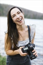 Portrait of woman holding camera by lake