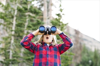 Boy (6-7) using binoculars in forest