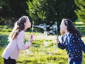 Girls (10-11, 12-13) blowing bubbles in field