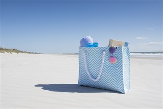 Bag with towel, book and sunglasses on empty beach