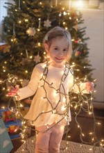 Little girl (4-5) wrapped with christmas lights in living room