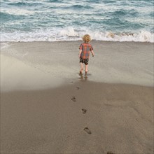 Rear view of little boy (2-3) walking on sandy beach