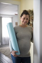 Pregnant woman standing in doorway and holding exercising mat