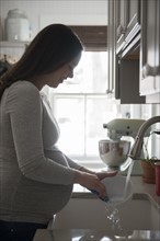 Pregnant woman washing bowl in kitchen sink