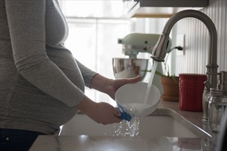 Pregnant woman washing bowl in kitchen sink, mid section