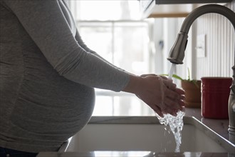 Pregnant woman washing hands in kitchen sink