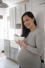 Pregnant woman standing in kitchen, holding bowl