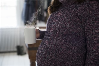 Pregnant woman holding mug with hot beverage