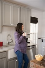 Pregnant woman standing in kitchen and holding mug