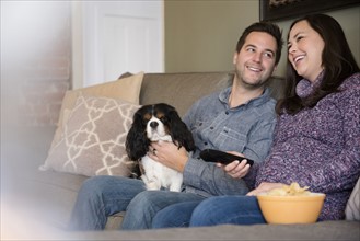 Happy mid adult couple relaxing on sofa with dog