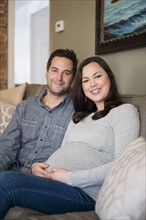 Mid adult couple sitting on sofa and smiling to camera