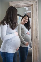 Pregnant woman looking in mirror, touching belly