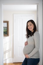 Portrait of pregnant woman standing in doorway, touching belly