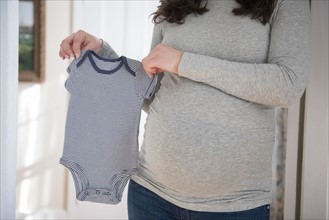 Pregnant woman holding infant bodysuit