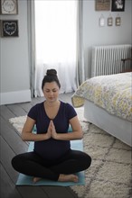 Pregnant woman doing yoga in bedroom