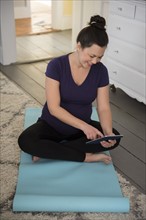 Pregnant woman sitting on yoga mat and using tablet pc