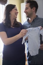 Pregnant woman holding infant bodysuit and smiling to man