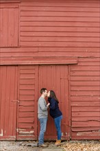 Couple kissing in front of red barn