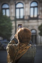 Spain, Andalusia, Seville, Plaza Nueva, Woman taking photo of building with smartphone