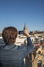 Spain, Andalusia, Seville, Plaza Nueva, Woman taking photo of cityscape and la Giralda with smartphone
