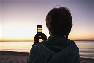 Woman on beach taking photo with smartphone