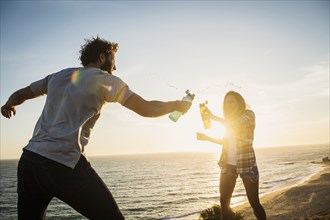 Couple having water fight on beach at sunset