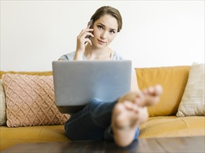 Woman using laptop and smart phone on sofa