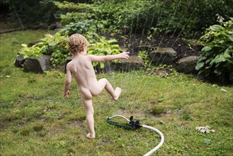 Naked boy playing with sprinkler