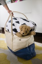 Girl's hand holding bag with blanket and teddy bear