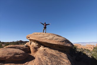 Man with arms outstretched on rock in Arches National Park, Utah, USA