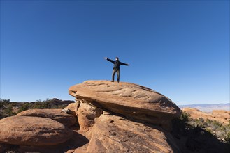 Man with arms outstretched on rock in Arches National Park, Utah, USA