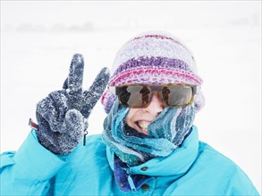 Smiling woman making peace gesture in snow
