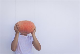 Young man holding pumpkin over his face