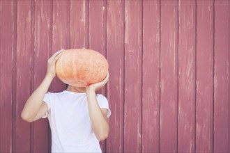 Young man holding pumpkin over his face